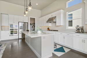 Kitchen with under cabinet range hood, stainless steel appliances, white cabinets, light countertops, and a high ceiling
