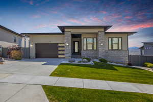 View of front of property with an attached garage, driveway, stone siding, and stucco siding
