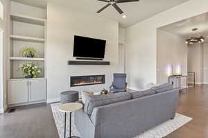 Living area with a glass covered fireplace, wood finished floors, baseboards, built in features, and ceiling fan
