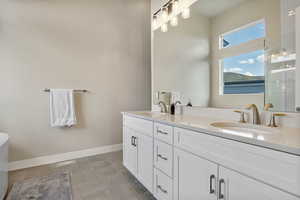 master bath with double vanity, tiled shower, and baseboards