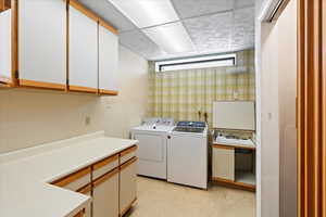 Laundry room with cabinet space, washing machine and clothes dryer, and wallpapered walls