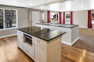 Kitchen featuring stainless steel microwave, a kitchen island, dark countertops, wood-type flooring, and baseboards