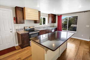 Kitchen featuring stainless steel appliances, a sink, baseboards, light wood-style floors, and a center island