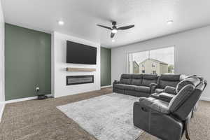 Living area with carpet flooring, a glass covered fireplace, a ceiling fan, recessed lighting, and baseboards