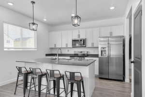 Kitchen featuring stainless steel appliances, a sink, light wood finished floors, dark countertops, and an island with sink