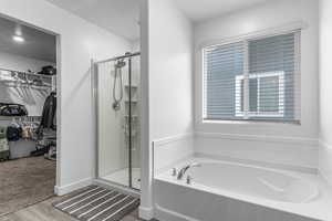 Full bathroom featuring a stall shower, a spacious closet, wood finished floors, and a garden tub