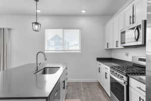 Kitchen with appliances with stainless steel finishes, a sink, light wood-style floors, dark countertops, and white cabinetry