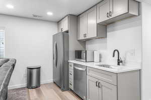 Kitchen with appliances with stainless steel finishes, a sink, gray cabinetry, light countertops, and recessed lighting