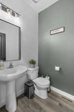Half bath with baseboards, toilet, wood finished floors, and a sink