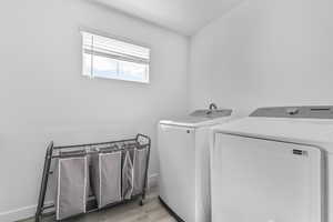 Clothes washing area featuring washer and dryer, light wood finished floors, and baseboards