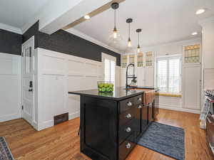 Kitchen with a decorative wall, ornamental molding, wallpapered walls, dark countertops, and dark cabinets