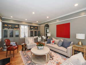 Living area with arched walkways, wood finished floors, ornamental molding, recessed lighting, and baseboards