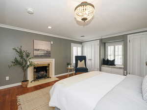 Bedroom with crown molding, wood finished floors, baseboards, two closets, and a fireplace