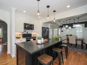 Kitchen featuring appliances with stainless steel finishes, arched walkways, white cabinets, backsplash, and light wood-type flooring