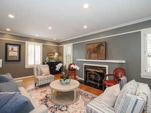 Living area featuring healthy amount of natural light, wood finished floors, a premium fireplace, recessed lighting, and ornamental molding