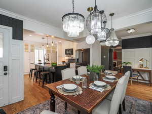 Dining area featuring a chandelier, wood finished floors, crown molding, arched walkways, and a decorative wall
