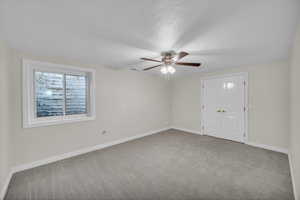 Empty room featuring carpet flooring, ceiling fan, baseboards, and a textured ceiling