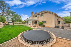 Rear view of house featuring a trellis covered patio, trampoline and firepit
