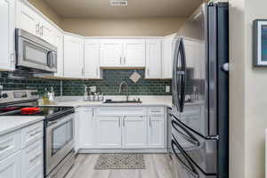 Kitchen featuring stainless steel appliances, a sink, white cabinetry, light countertops, and decorative backsplash
