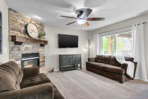 Carpeted living room with ceiling fan, a stone fireplace, and baseboards