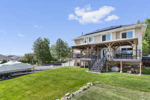 Rear view of house featuring solar panels, stairs, a wooden deck, a yard, and stucco siding