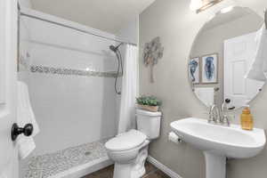 Bathroom featuring toilet, a tile shower, a sink, and baseboards