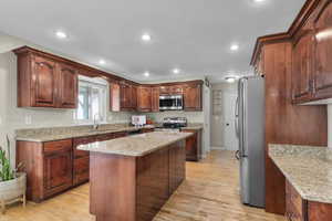 Kitchen with appliances with stainless steel finishes, a sink, light wood-style floors, recessed lighting, and a kitchen island