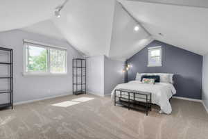 Carpeted bedroom featuring rail lighting, vaulted ceiling, and baseboards