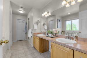 Bathroom with a chandelier, a shower stall, tile patterned floors, and double vanity