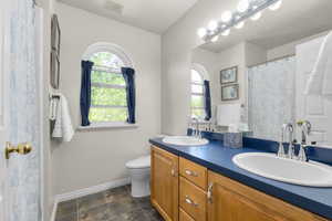 Bathroom with baseboards, toilet, and double vanity
