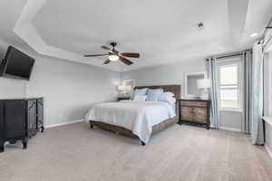 Carpeted bedroom with a tray ceiling, baseboards, and a ceiling fan