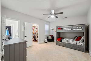 Bedroom with a walk in closet, light colored carpet, baseboards, a closet, and ceiling fan