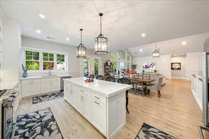 Kitchen featuring appliances with stainless steel finishes, a kitchen island, white cabinetry, light wood-style floors, and light countertops