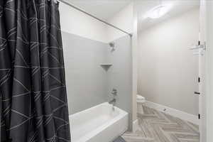 Bathroom with baseboards, toilet, and shower / tub combo with curtain