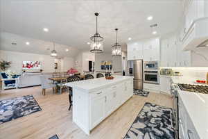 Kitchen with appliances with stainless steel finishes, a kitchen bar, light wood-type flooring, light countertops, and recessed lighting