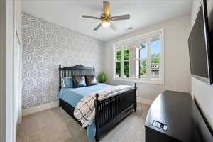 Carpeted bedroom featuring wallpapered walls, baseboards, an accent wall, and a ceiling fan