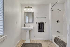 Bathroom with tile patterned flooring, washtub / shower combination, baseboards, and a sink