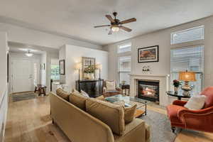 Living room with a fireplace, a ceiling fan, light wood finished floors, and baseboards