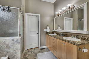 Full bathroom with a shower stall, double vanity, baseboards, and stone finish flooring