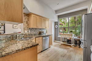 Kitchen featuring stainless steel appliances, a sink, light brown cabinets, tasteful backsplash, and light stone countertops
