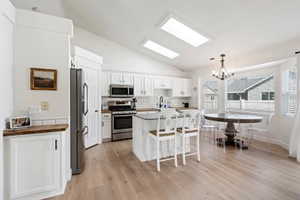 Kitchen featuring appliances with stainless steel finishes, vaulted ceiling, a breakfast bar area, a chandelier, and light wood-style flooring