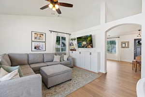 Living room with arched walkways, wood finished floors, ceiling fan, and lofted ceiling