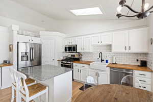 Kitchen with stainless steel appliances, butcher block countertops, a sink, vaulted ceiling, and tasteful backsplash