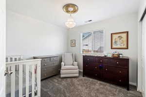 Bedroom with dark colored carpet, a chandelier, a nursery area, and baseboards