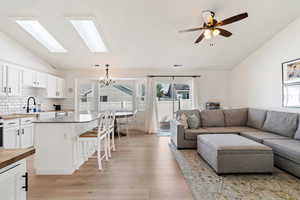 Living area with vaulted ceiling, a chandelier, light wood-style floors, and a ceiling fan