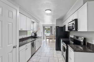 Kitchen featuring stainless steel appliances, a sink, white cabinetry, tile floors and granite countertops