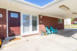 View of exterior entry featuring brick siding and a patio area