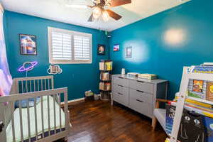 Bedroom with a textured ceiling, wood finished floors, a crib, ceiling fan, and baseboards