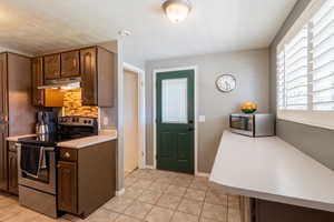 Kitchen featuring stainless steel appliances, under cabinet range hood, light countertops, decorative backsplash, and light tile patterned flooring