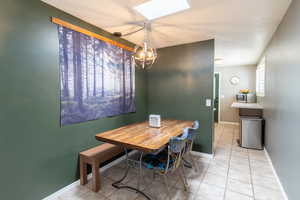 Dining area with a skylight, a chandelier, light tile patterned floors, and baseboards